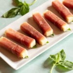 Closer view of white platter holding colorful prosciutto wrapped mozzarella sticks.