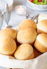 basket of quick dinner rolls with salt and pepper, plates, a candle and a salad in the background