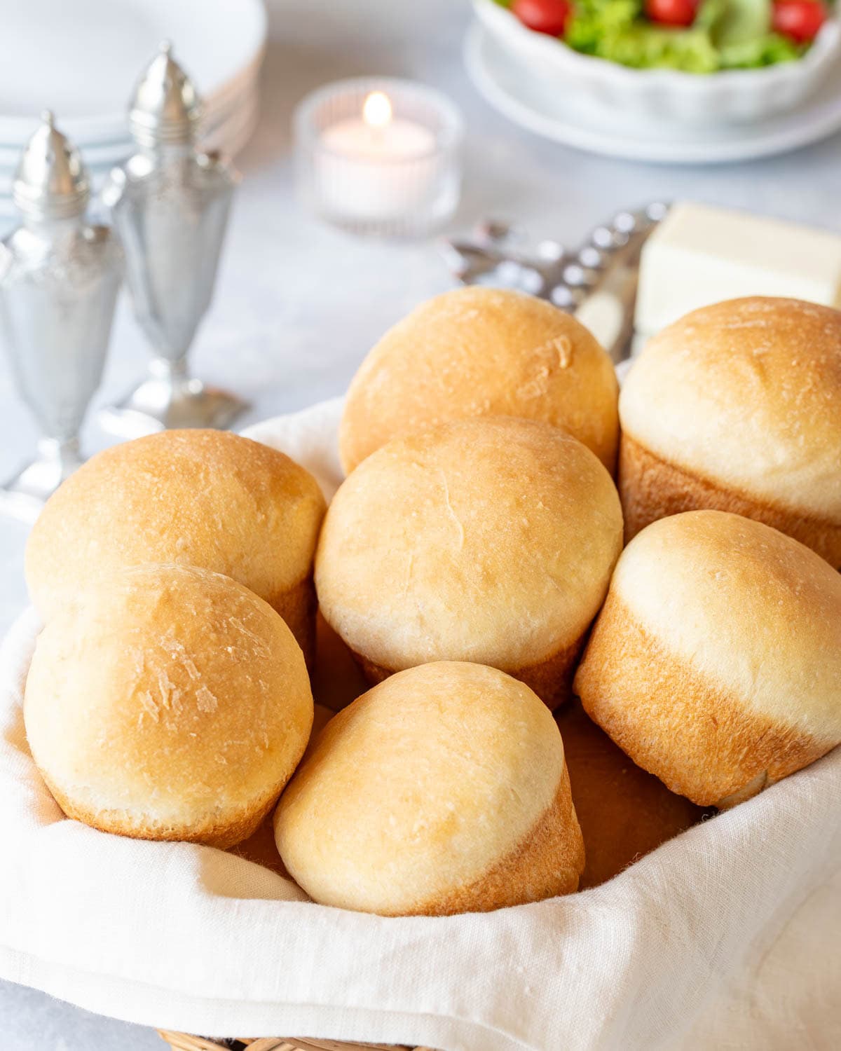 basket of quick dinner rolls with salt and pepper, plates, a candle and a salad in the background