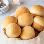 close up of quick dinner rolls in a basket with plates and cutlery in the background