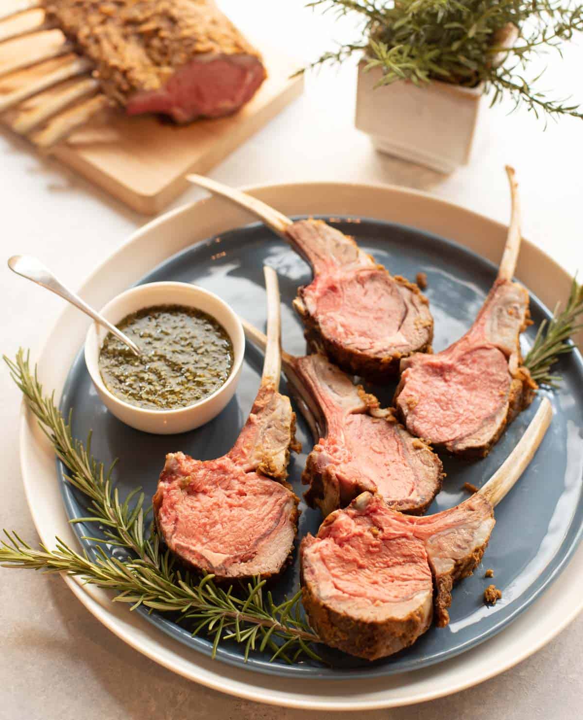 Blue plate with Mustard Crusted Rack of Lamb, sliced, with Fresh Mint Sauce on the side