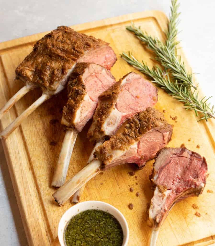 cutting board with sliced Mustard Crusted Rack of Lamb with Fresh Mint Sauce on the side