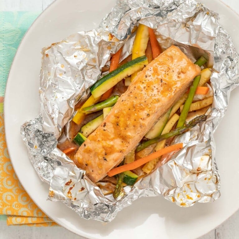 overhead view of salmon and vegetables baked in foil, with foil cut open to show inside