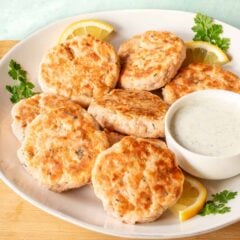 round plate holding several salmon patties, along with a bowl of Tzatziki sauce on the side.