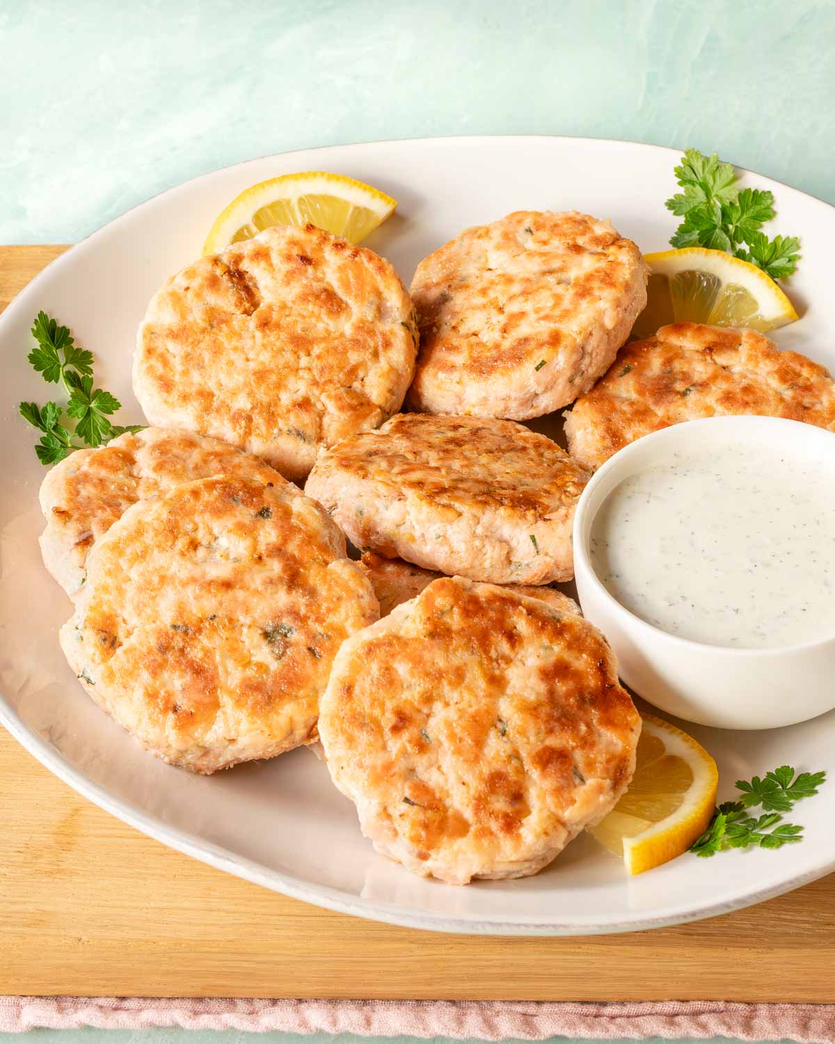 round plate holding several salmon patties, along with a bowl of Tzatziki sauce on the side.