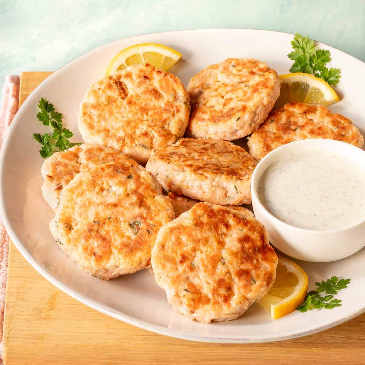 round plate holding several salmon patties, along with a bowl of Tzatziki sauce on the side