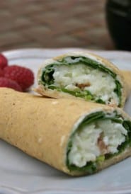 blue plate holding 1 stuffed crepe, cut in half to show the ham, scrambled egg, and spinach inside.