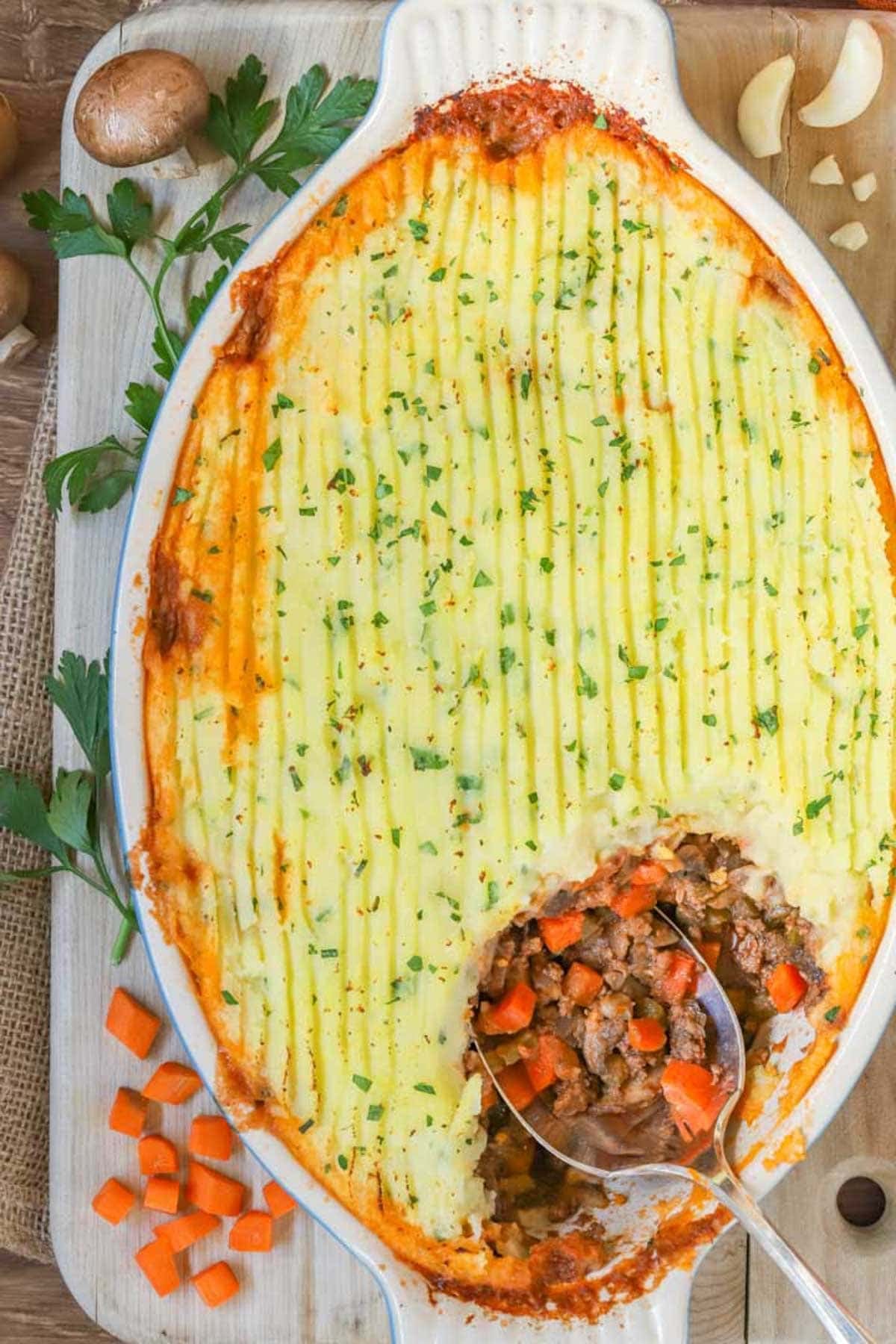 overhead view of an oval baking dish filled with Shepherd's PIe, with one corner scooped out showing the filling.