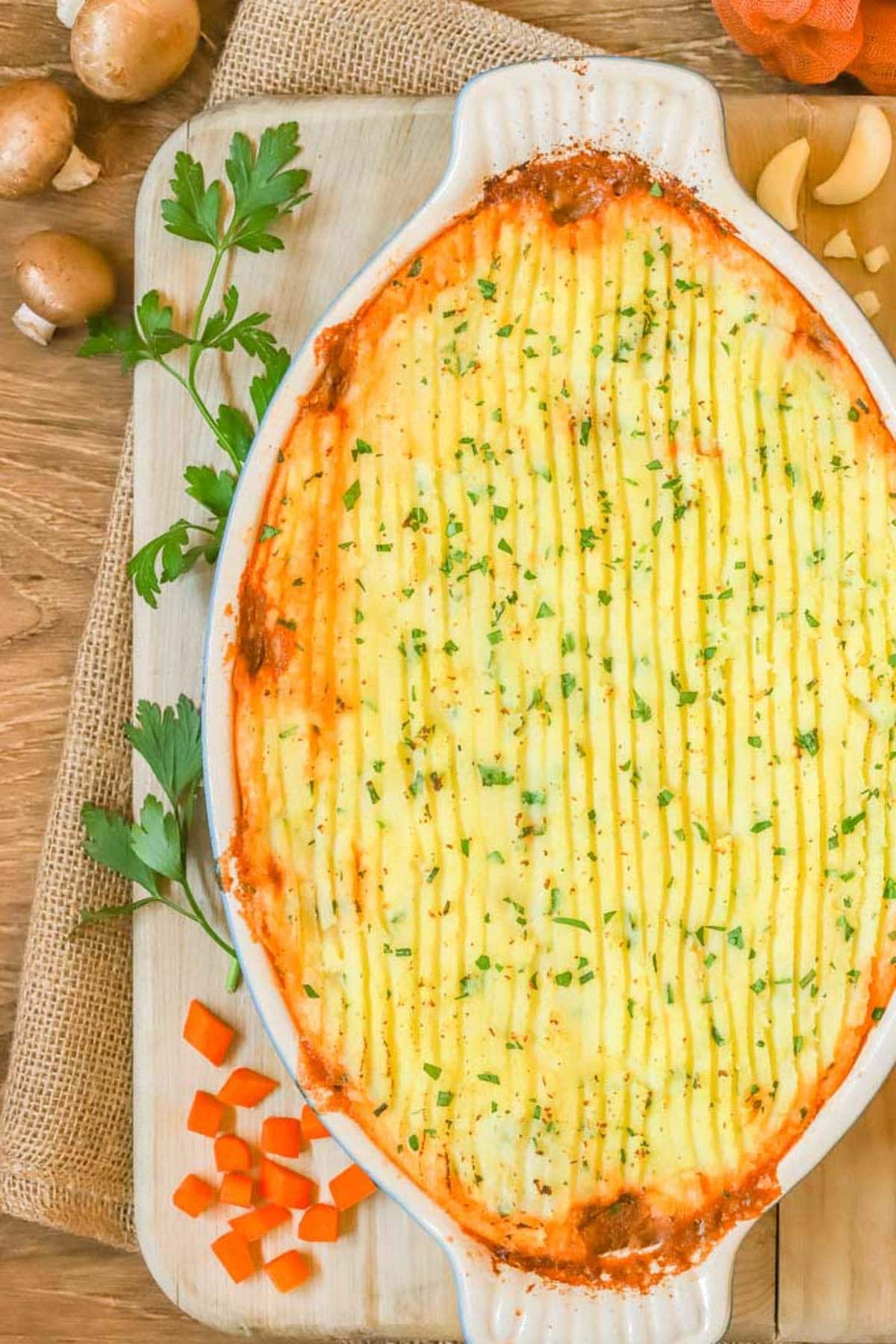 overhead shot of a shepherd's pie, surrounded by mushrooms, chopped cararots, garlic and parsley.