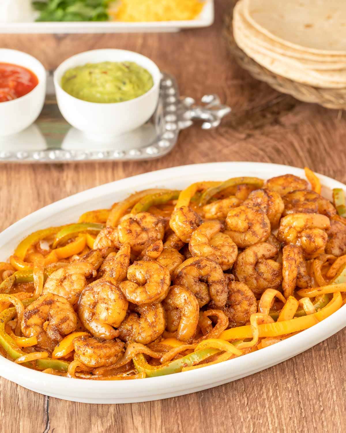 White oval platter holding shrimp fajitas with various toppings and tortillas in the background