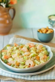 Chopped Shrimp Salad with Rice and Avocado mounded on top of a blue plate, with cashews and a pitcher if flowers in the background