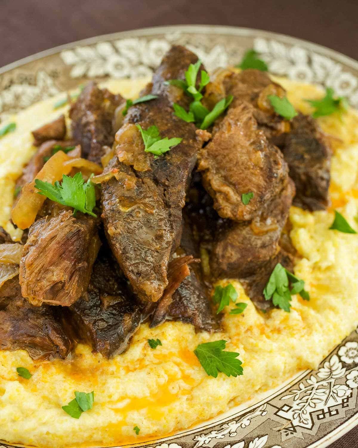 Brown and white plate holding creamy polenta with slow cooker beef short ribs and sauce on top.