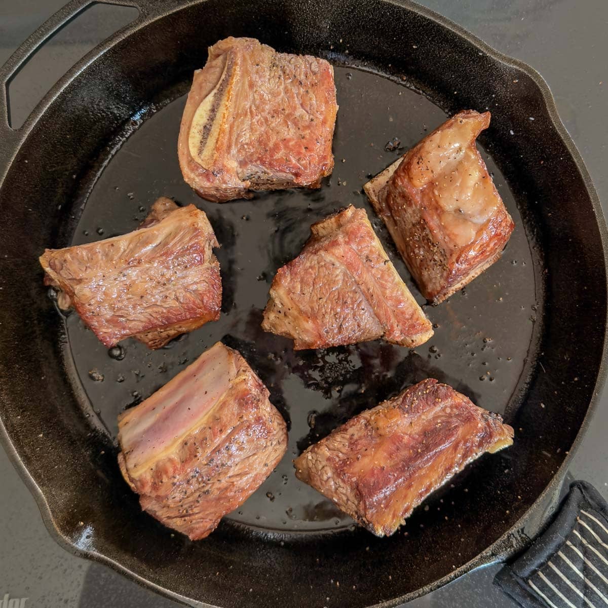 Searing bone-in beef short ribs in a cast iron skillet to lock in flavor.