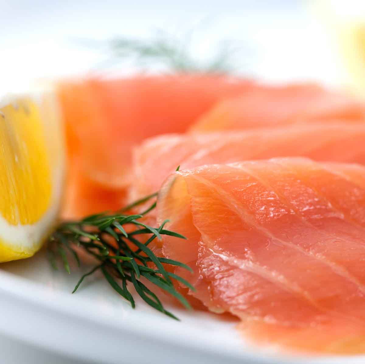 rolled pieces of smoked salmon on a white platter with dill and a lemon slice