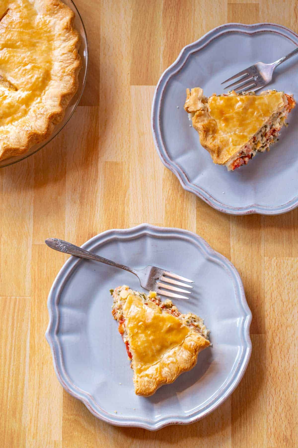 Two blue plates with slices of Southern Tomato Pie. Portion of whole pie in upper left corner