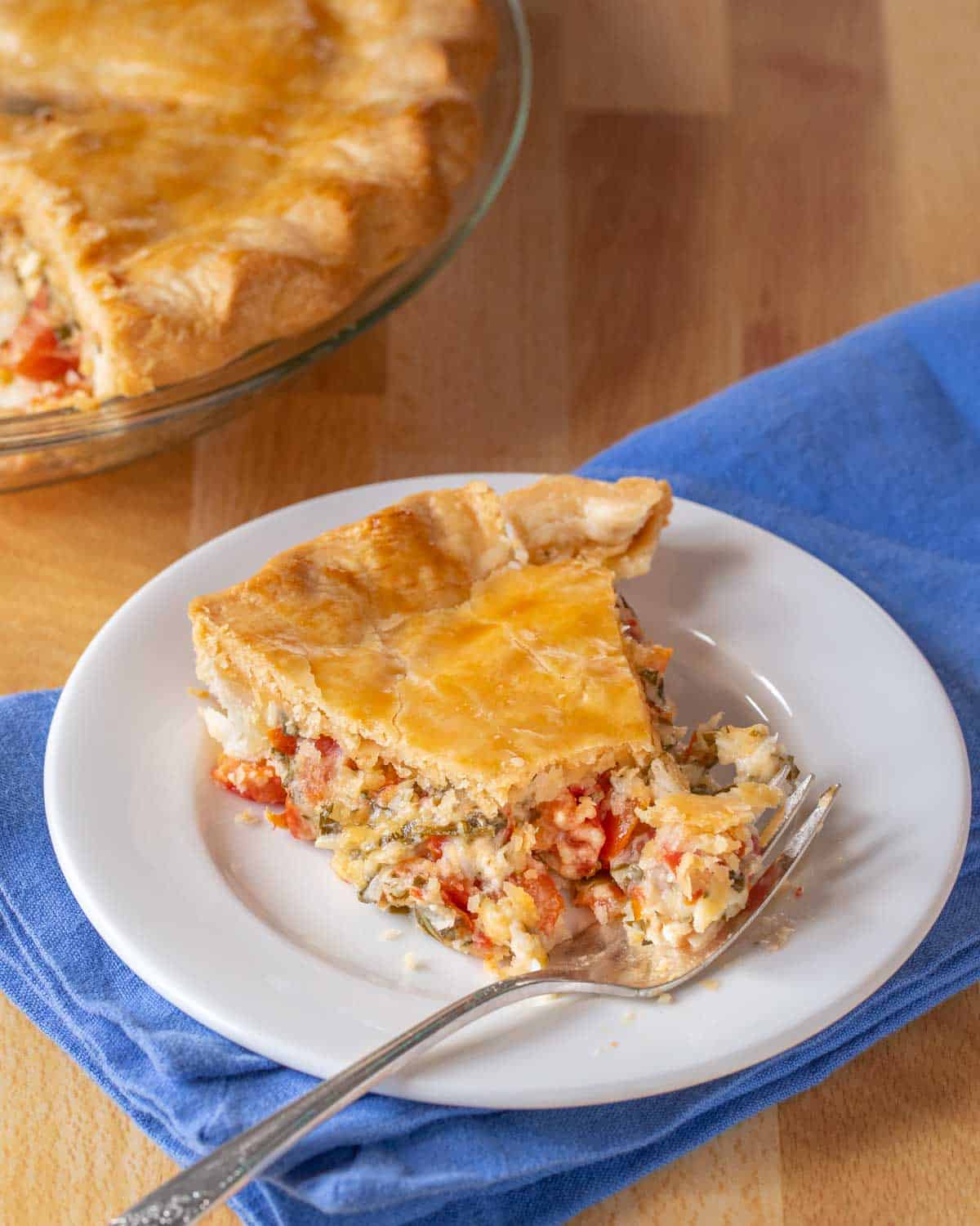 Slice of Southern Tomato Pie showing inside, with whole pie in background