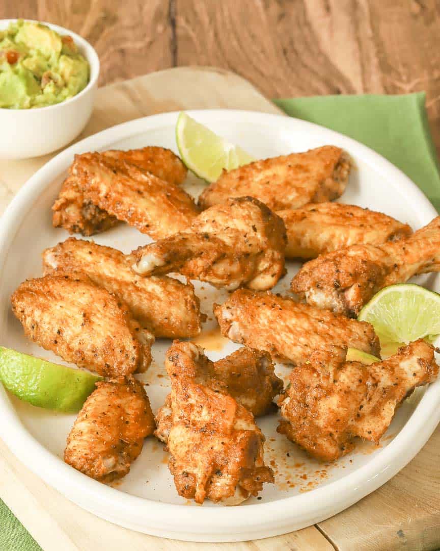 overhead shot of round oval white platter filled with spicy chicken wings; guacamole in a bowl on the side