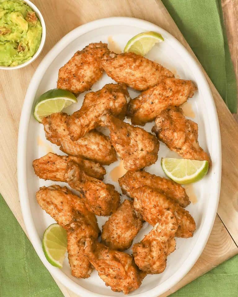 overhead shot of a large oval white platter filled with spicy chicken wings; guacamole in a bowl on the side.