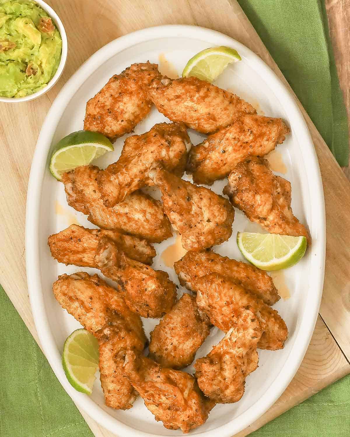 Large oval white platter filled with spicy, juicy chicken wings; chunky guacamole in a bowl on the side.