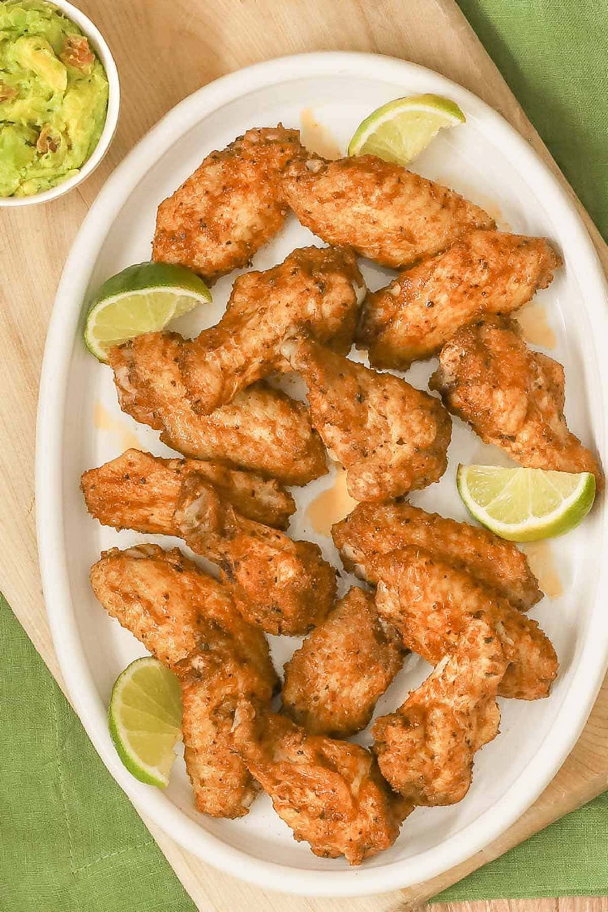 Large oval white platter filled with spicy, juicy chicken wings; chunky guacamole in a bowl on the side