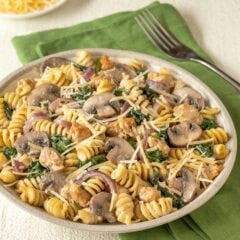 Closer view of a bowl holding a large portion of chicken sausage, spinach, and mushroom pasta, with grated Parmesan