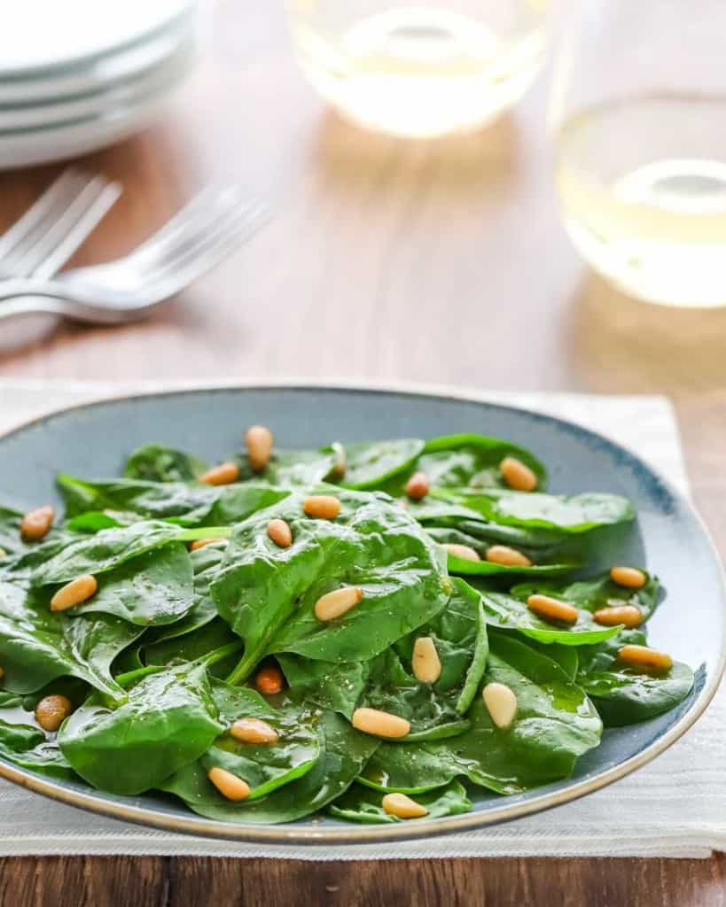 blue plate holding a serving of Easy Spinach Salad with wine glasses, forks and plates in the background