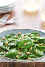 blue plate holding a serving of Easy Spinach Salad with wine glasses, forks and plates in the background