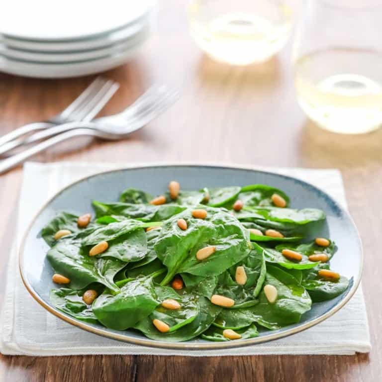 blue plate holding a serving of Easy Spinach Salad with wine glasses, forks and plates in the background