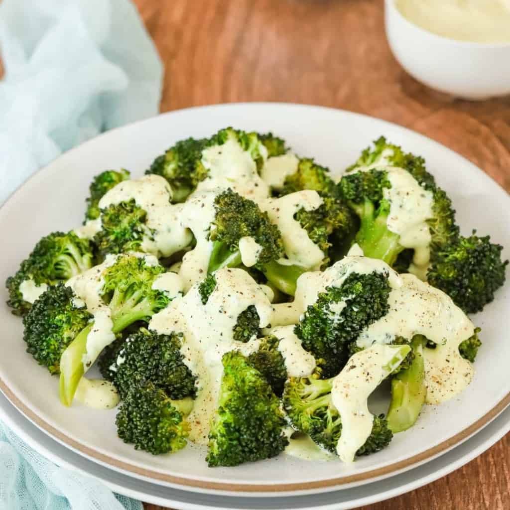 white plate holding steamed broccoli drizzled with curry mayo