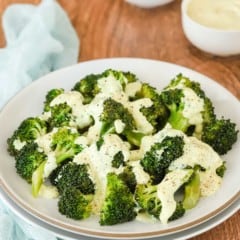 white plate holding steamed broccoli with lemon and curry mayo sauce