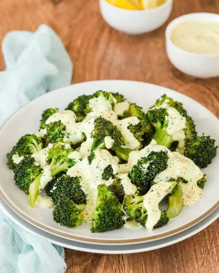 white plate holding steamed broccoli with lemon and curry mayo sauce