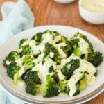 white plate holding steamed broccoli with lemon and curry mayo sauce.