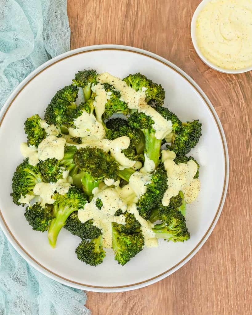 overhead shot of white plate holding steamed broccoli drizzled with curry mayo sauce, with more sauce on the side