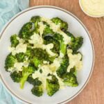 overhead shot of white plate holding steamed broccoli drizzled with curry mayo sauce, with more sauce on the side.