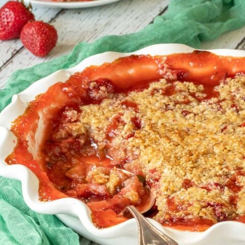 Strawberry Rhubarb Crisp in a white pie plate with a scoop removed, and a spoon in the plate