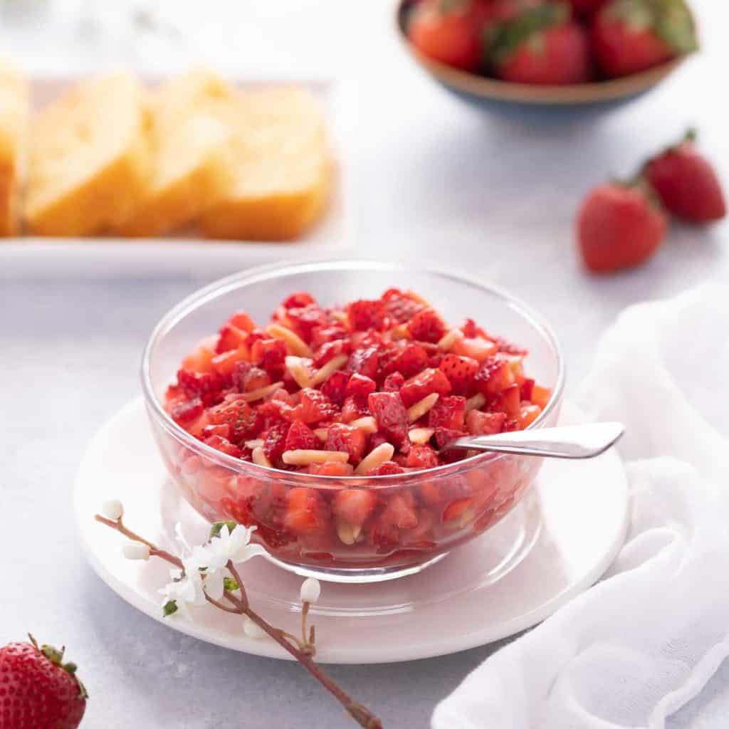 Close up of glass bowl showing Strawberry Topping, with sliced cake in the background