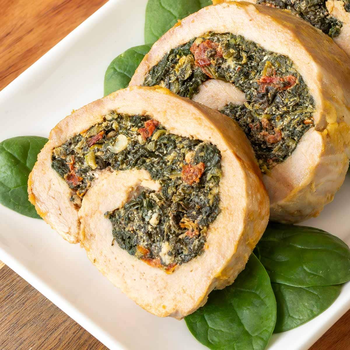 Close up of two slices of stuffed pork tenderloin on a white platter, garnished with baby spinach on the side