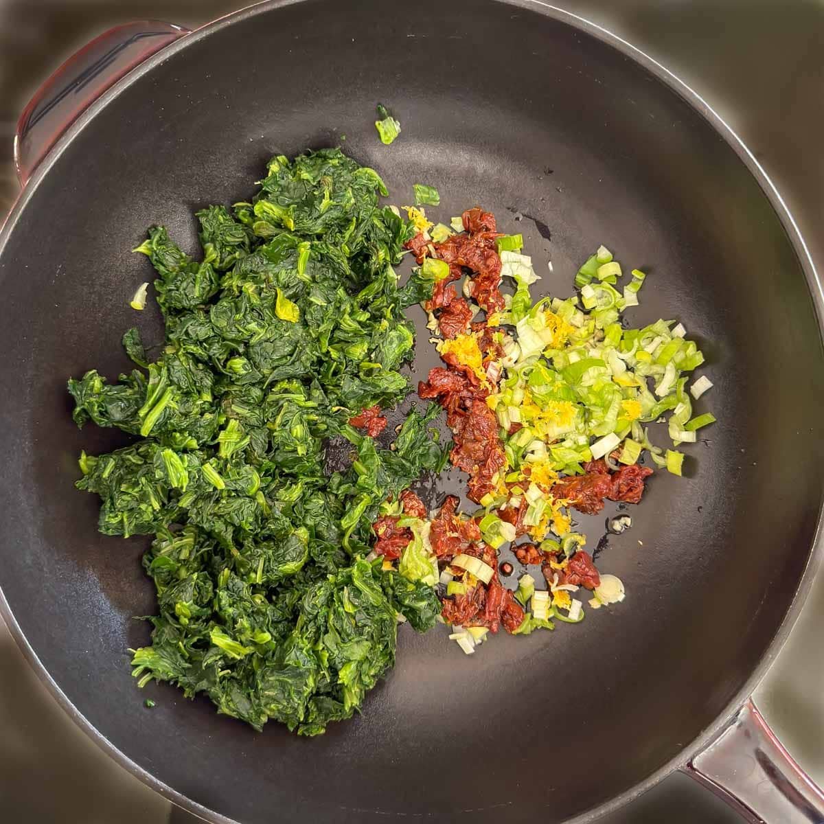 Spinach stuffing ingredients sitting in a large skillet, not stirred together.