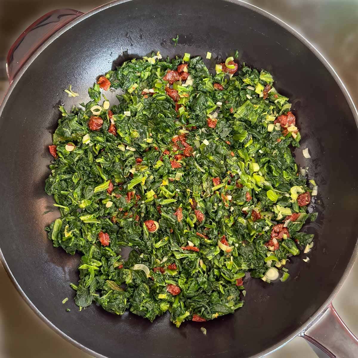 Spinach stuffing ingredients sautéing in a large skillet.