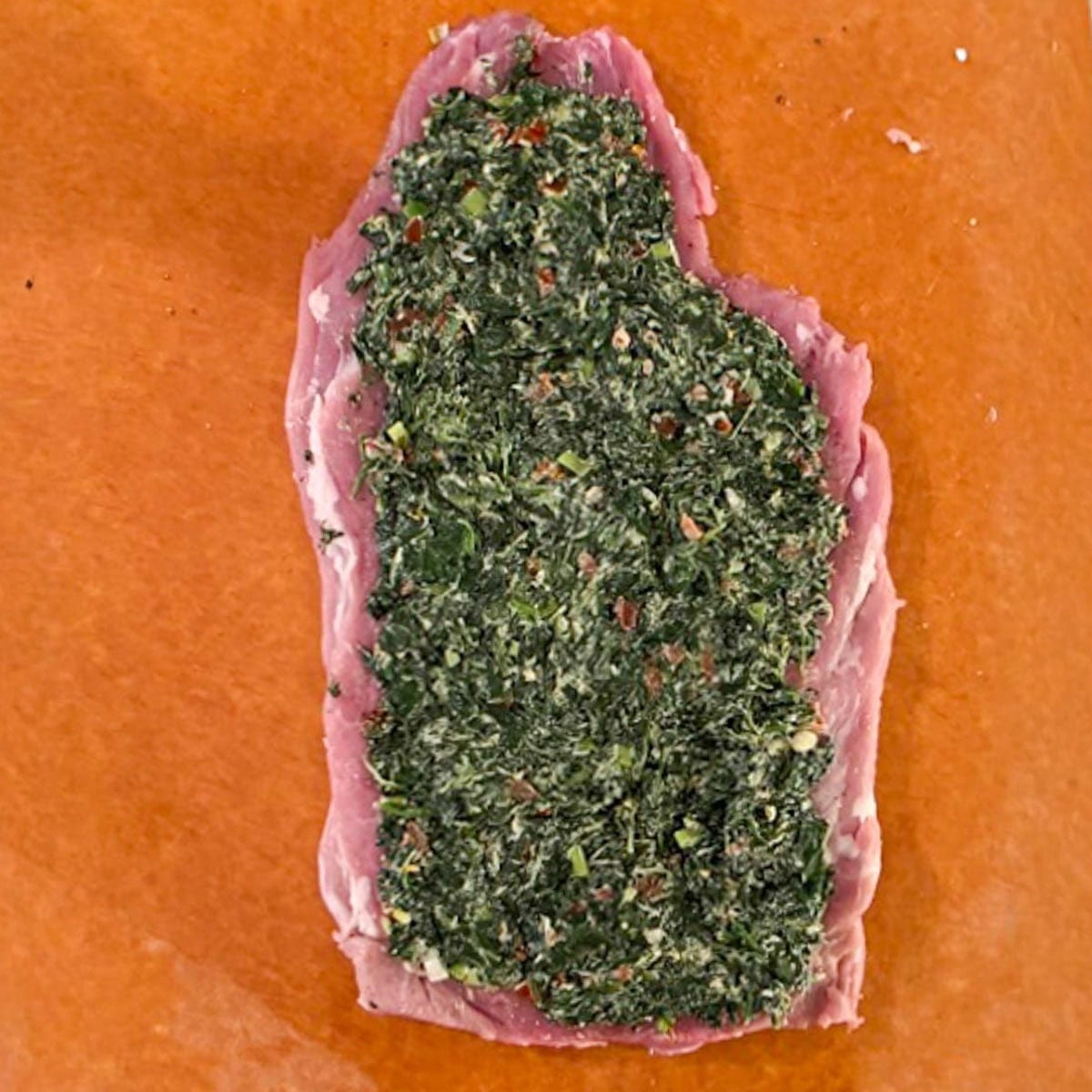 One pork tenderloin lying flat with spinach stuffing spread on top.
