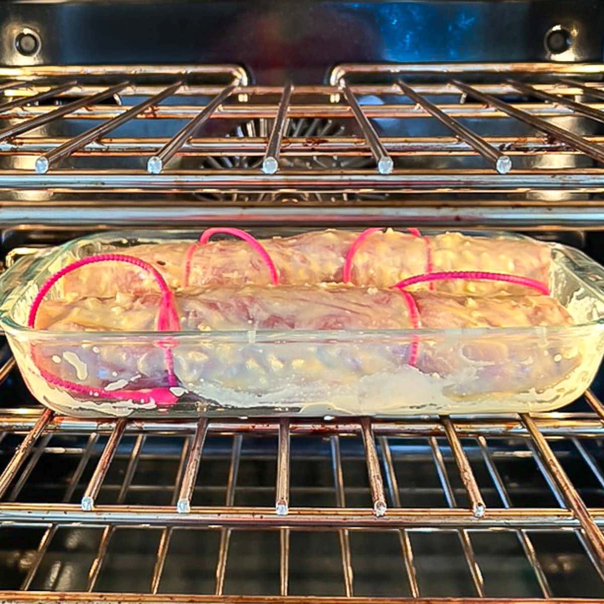 Two stuffed pork tenderloins brushed with basting sauce, in a baking dish in the oven.