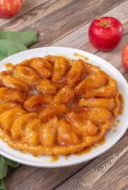 photo of Apple Tarte Tatin on a white plate, with 3 red apples in the background