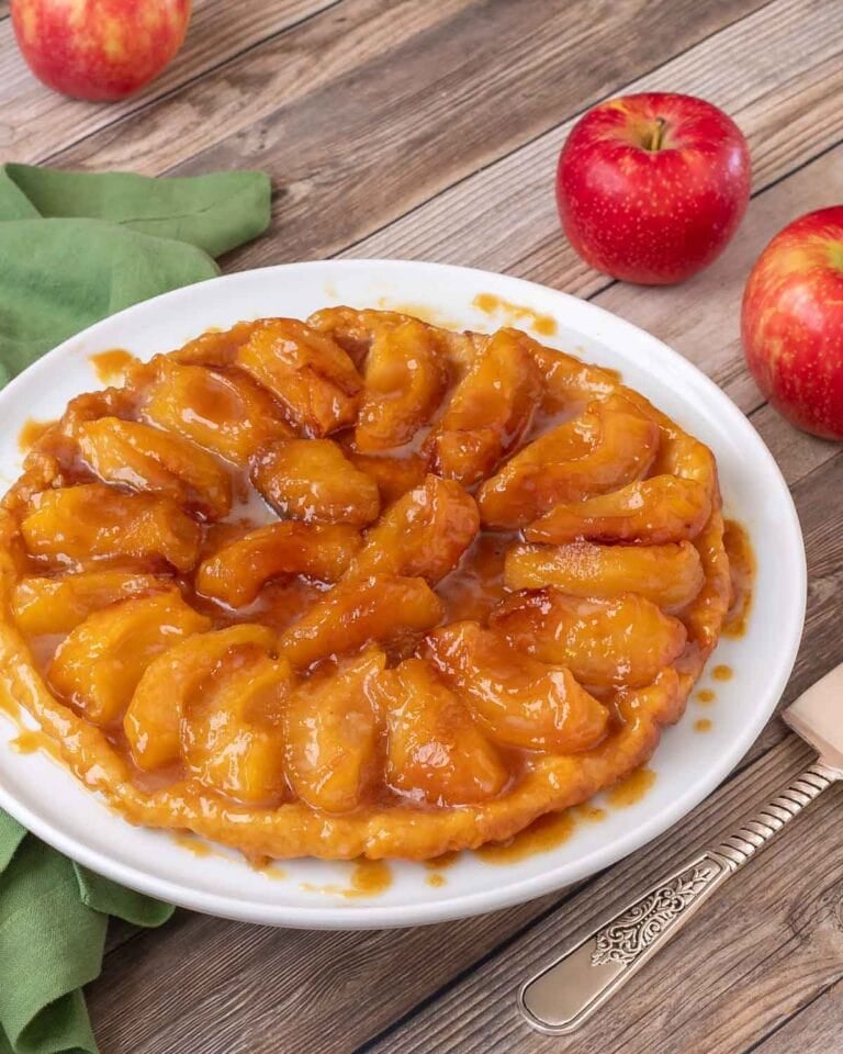 photo of Apple Tarte Tatin on a white plate, with 3 red apples in the background