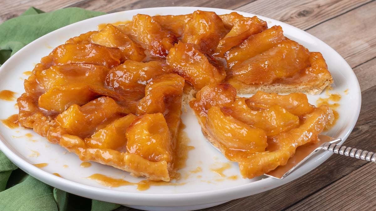 close up photo of Apple Tarte Tatin on a white plate, with one slice on a silver pie servier