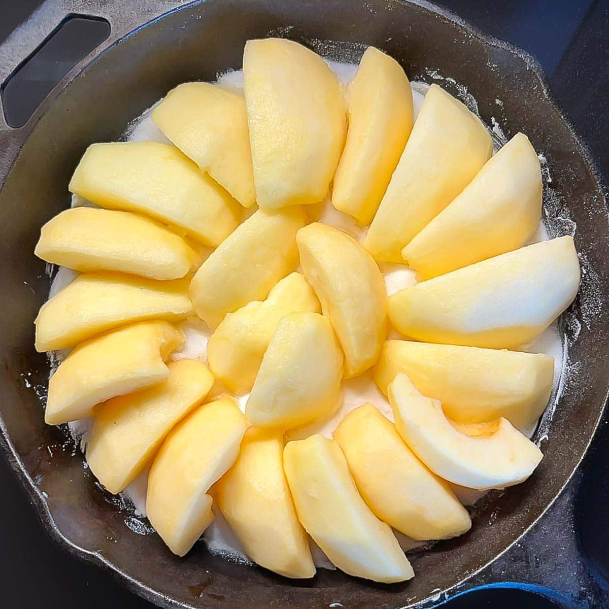 Apple quarters arranged in a circle atop sugar-butter mixture in skillet