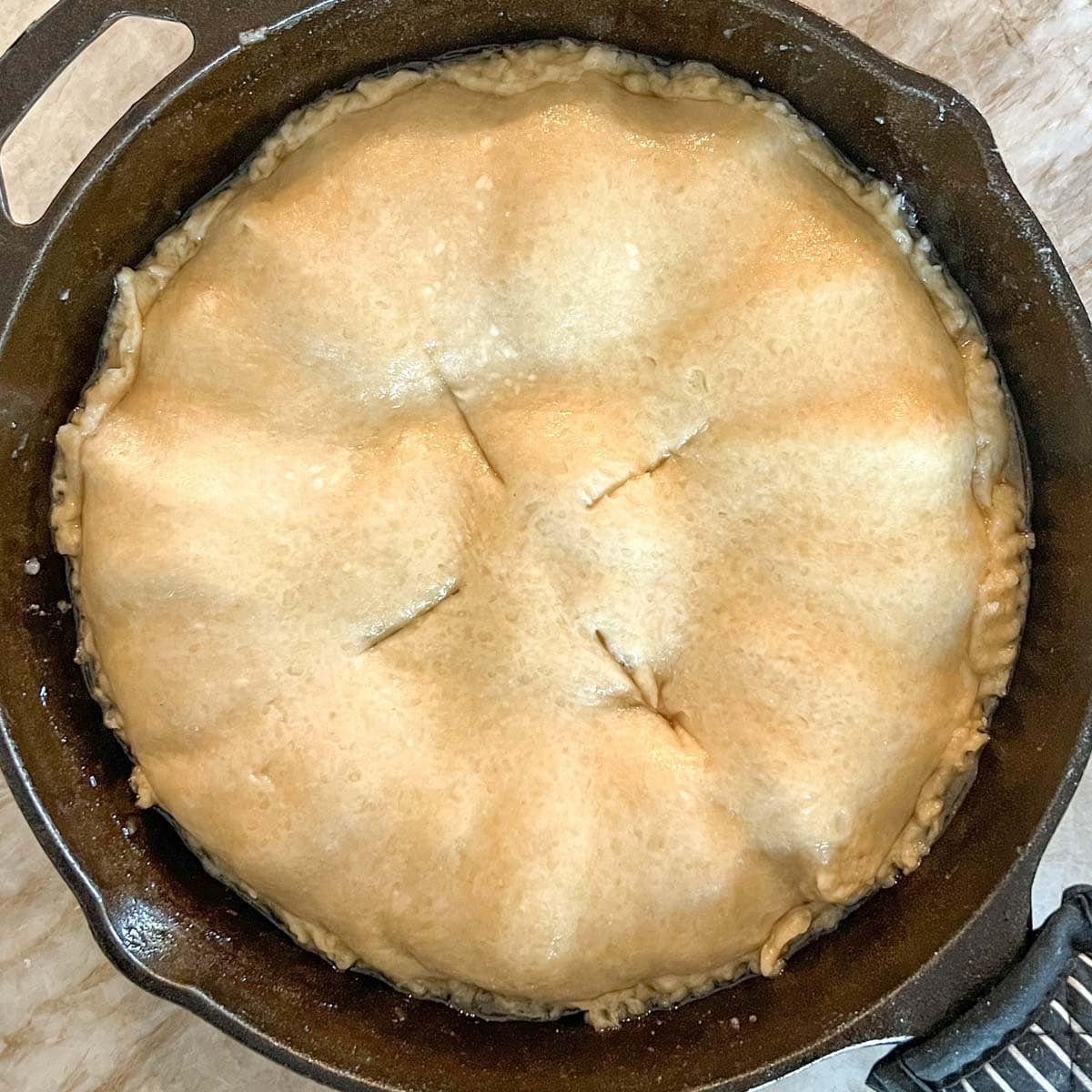 Placing dough for crust on top of apple caramel mixture, tucked in on the sides and with 4 small vent cuts