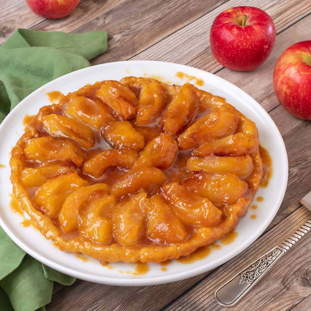 photo of Apple Tarte Tatin on a white plate, with 3 red apples in the background