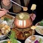 copper fondue pot holding tex mex fondue surrounded by chopped vegetables and bread for dipping.