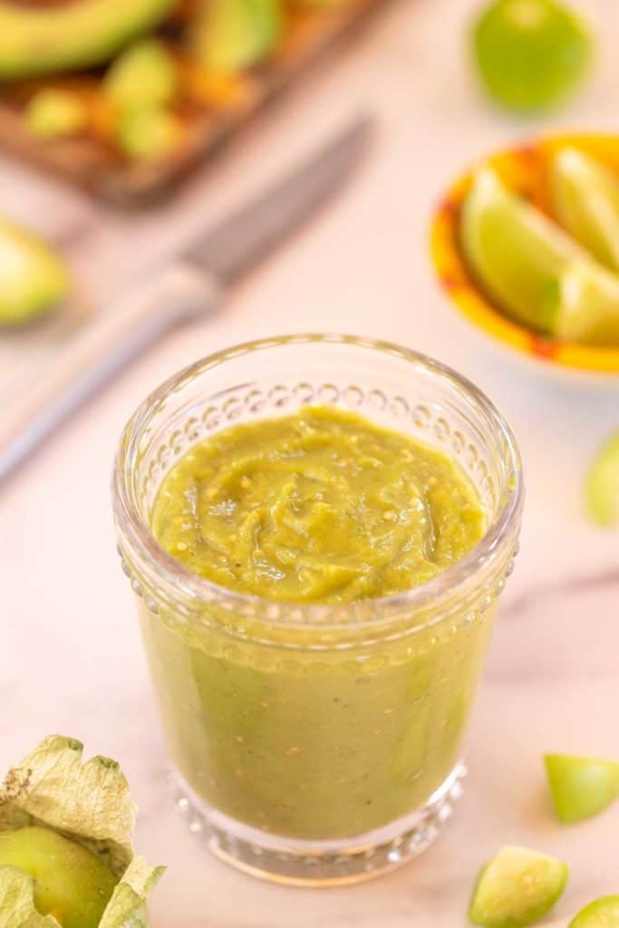 Clear glass filled with Tomatillo Avocado Sauce, surrounded by tomatillo and avocado pieces