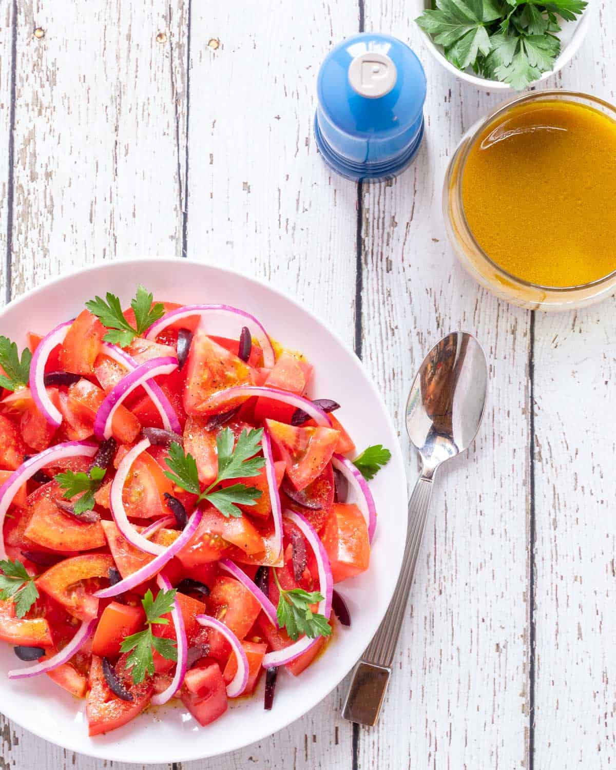 white plate showing Tomato Salad Recipe, with a spoon, Cumin Dressing and a pepper mill on the side.